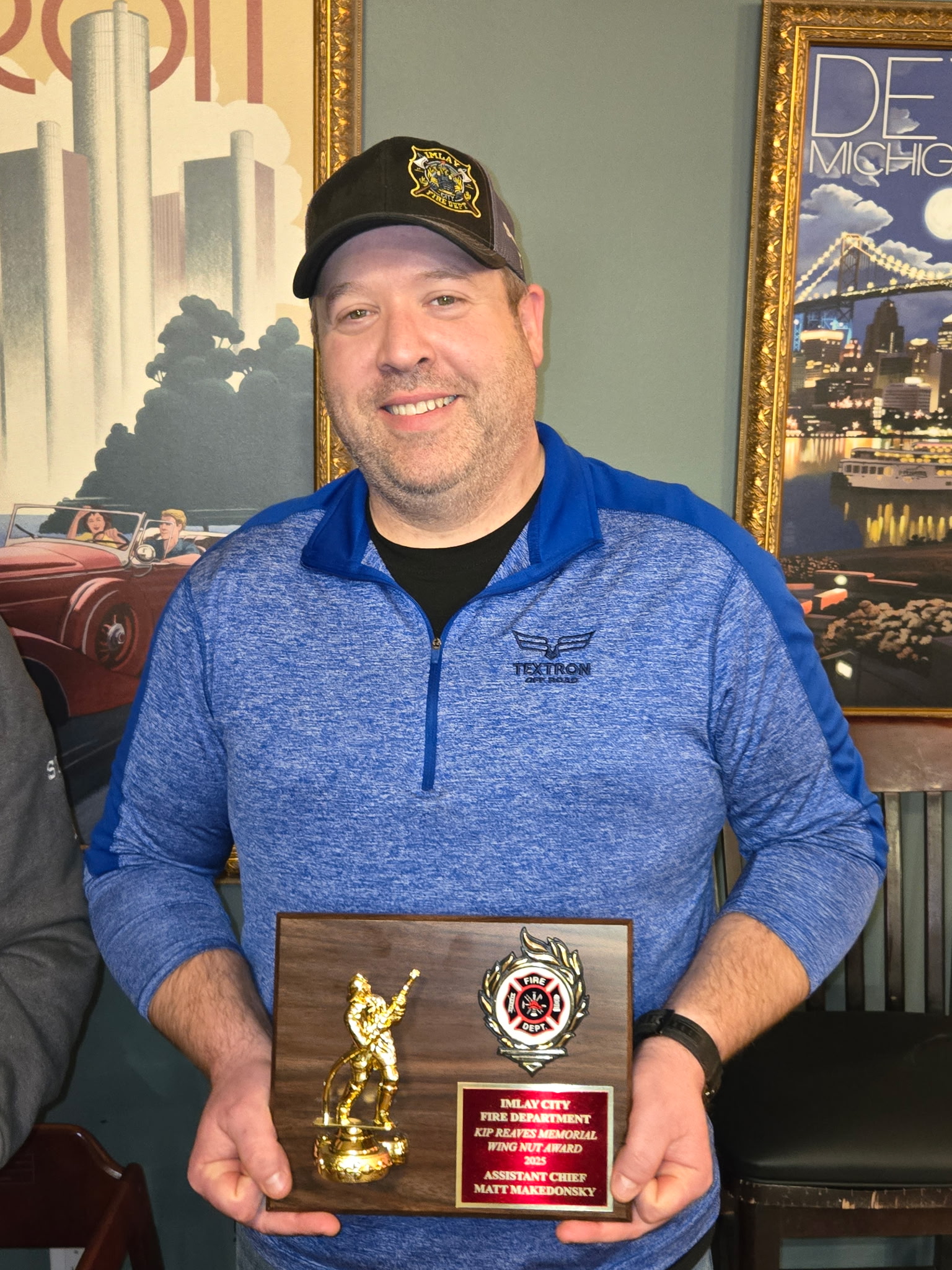 Person holding fire department award plaque, smiling.